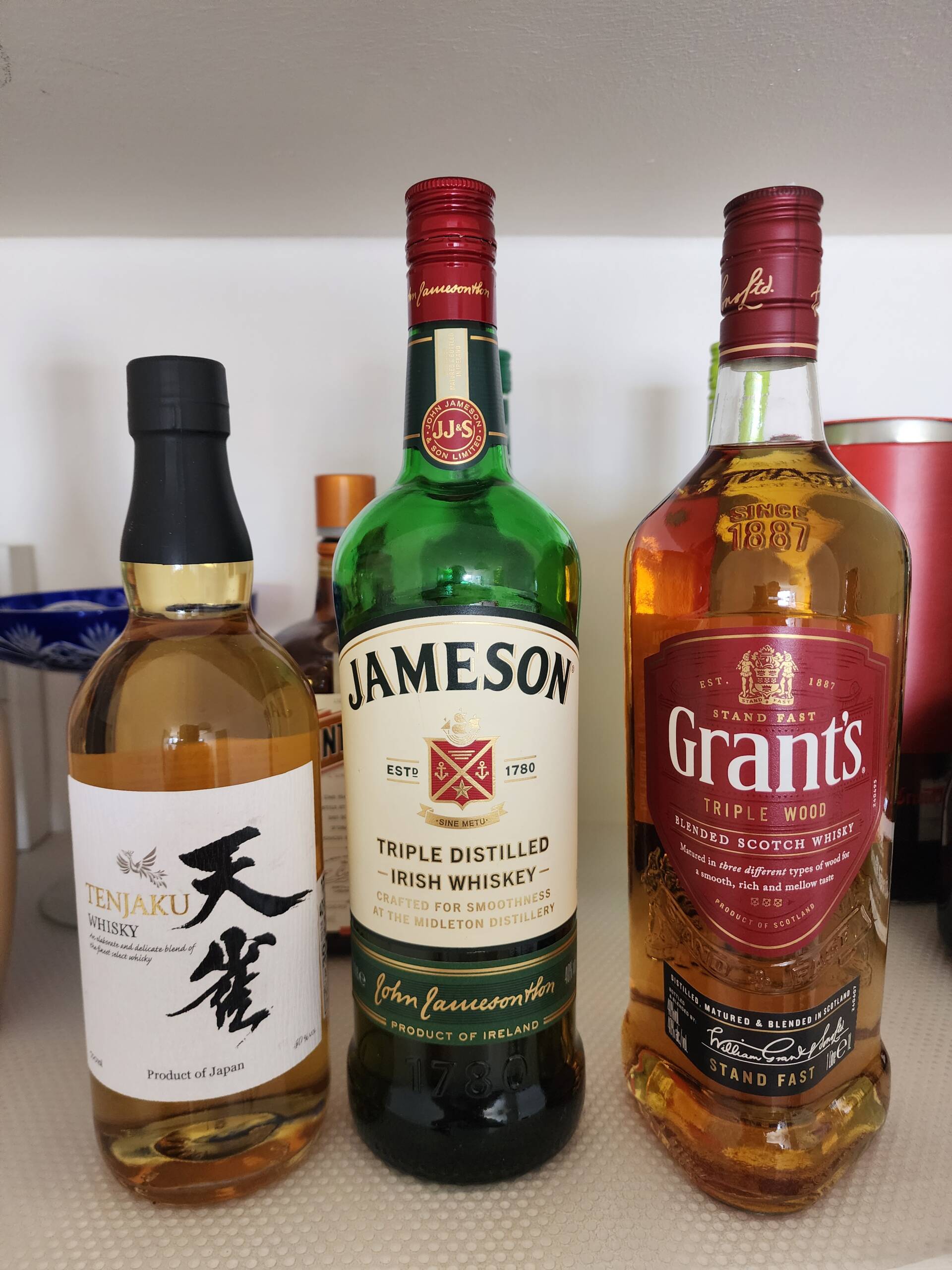 Three whisky bottles on a countertop — Tenjaku Japanese whisky, Jameson Irish Whiskey, and Grant&rsquo;s Triple Wood blended Scotch
