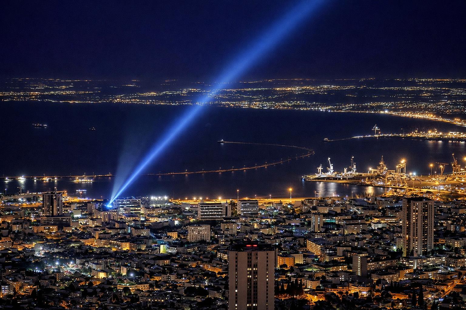 Night view over a bay, sodium-lit city below and a blue searchlight beam crossing the water