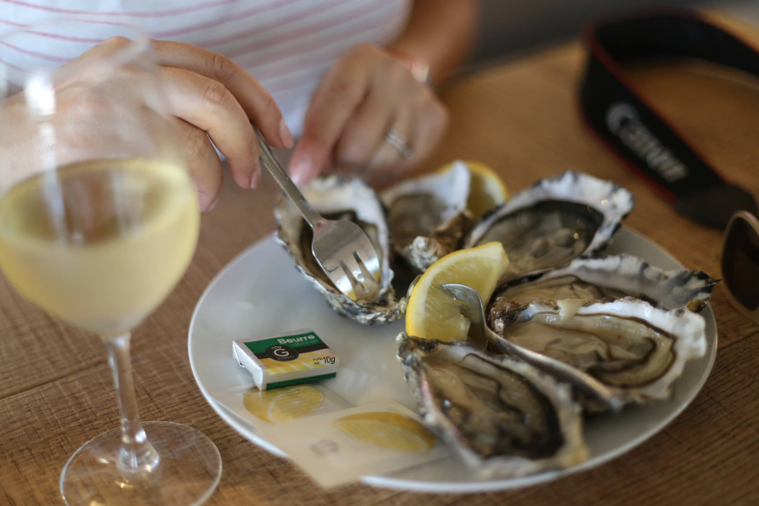 A plate of oysters with lemon wedges, a small pack of butter, and a glass of white wine