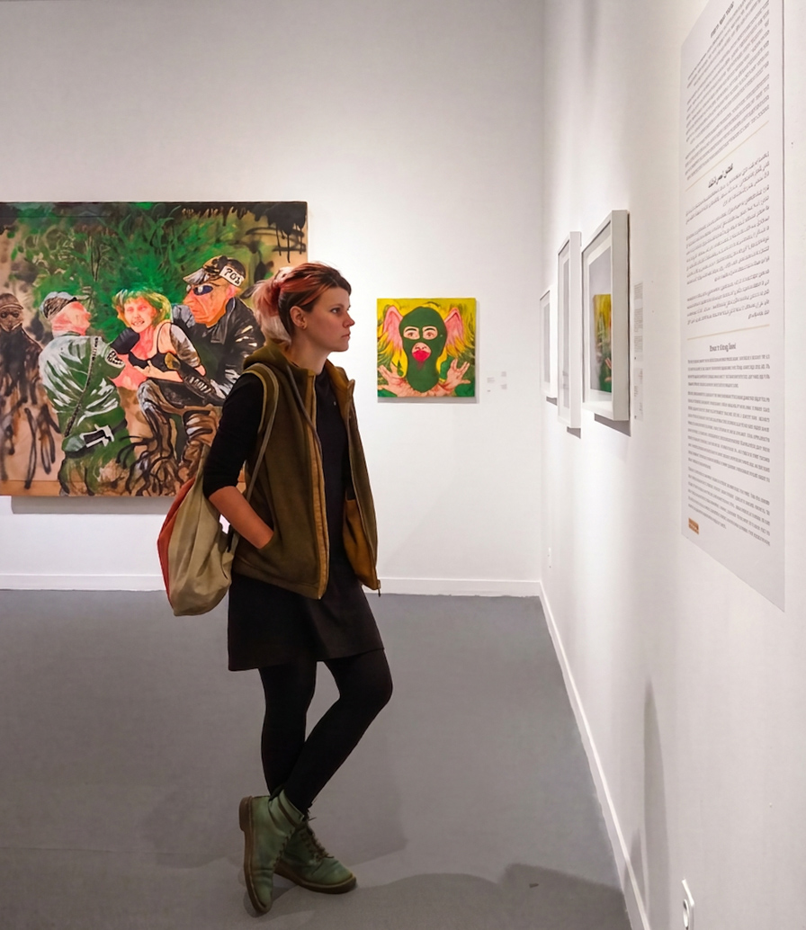 A gallery visitor pausing in front of a wall text panel, with paintings on the wall behind her