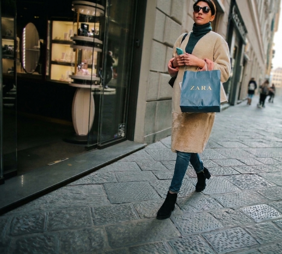 Woman in a cream shearling coat and black boots walking down an Italian shopping street