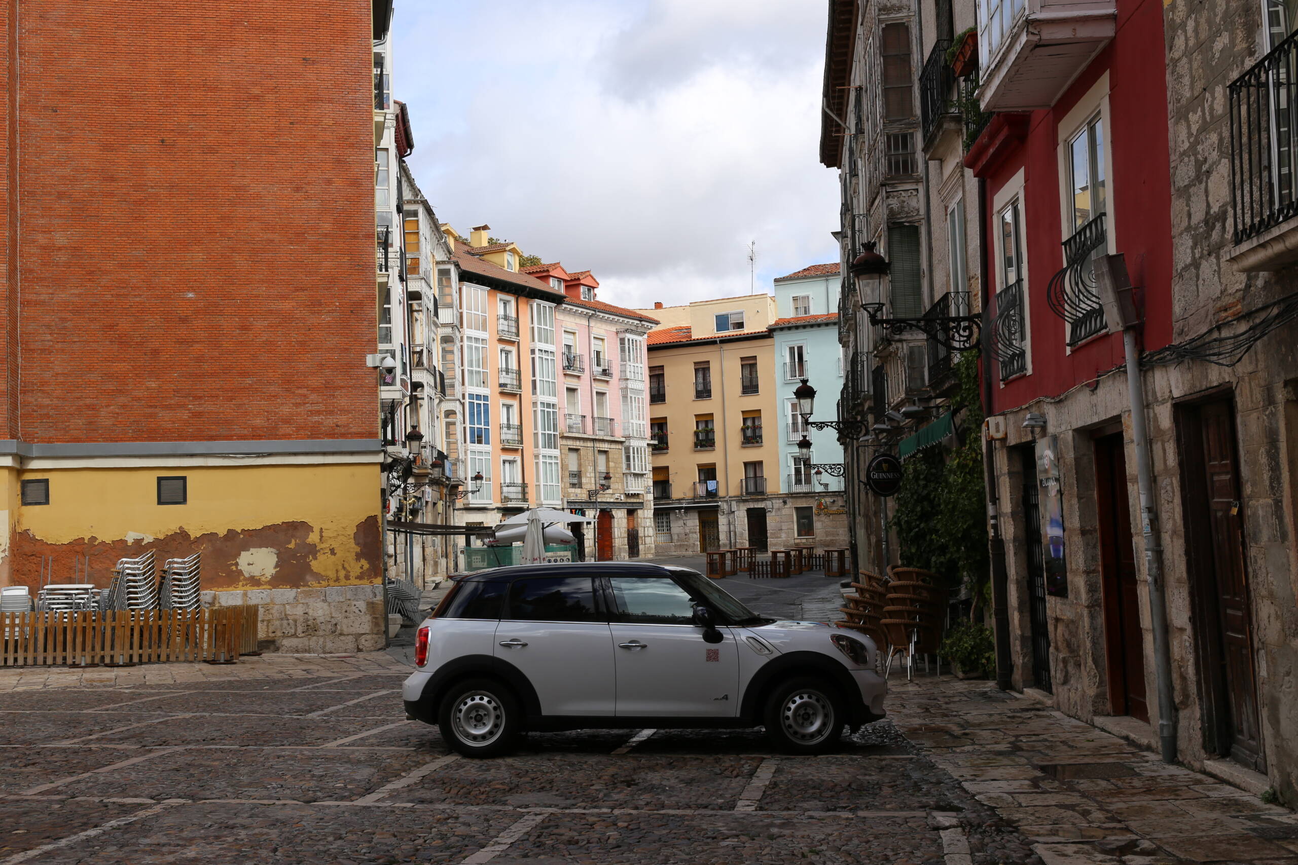An empty cobbled street in the old town of Burgos, colourful glazed miradores in the distance, a single parked car