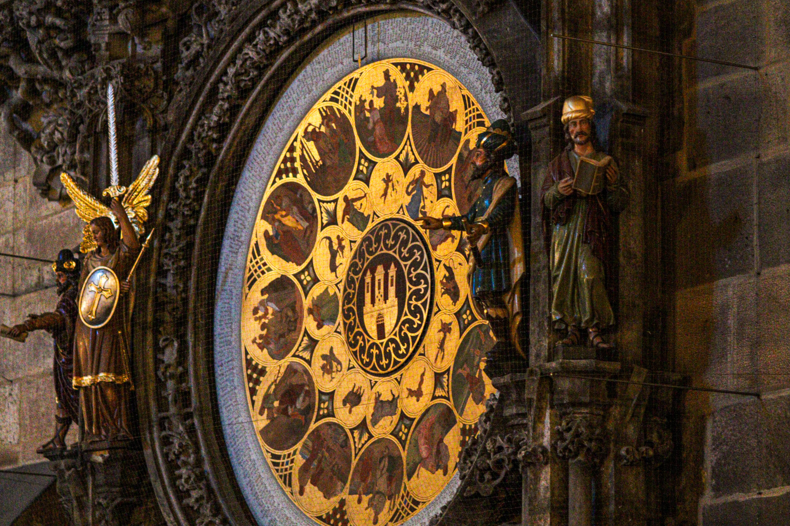The painted calendar dial of the Prague astronomical clock at night, with the archangel and chronicler figures flanking it