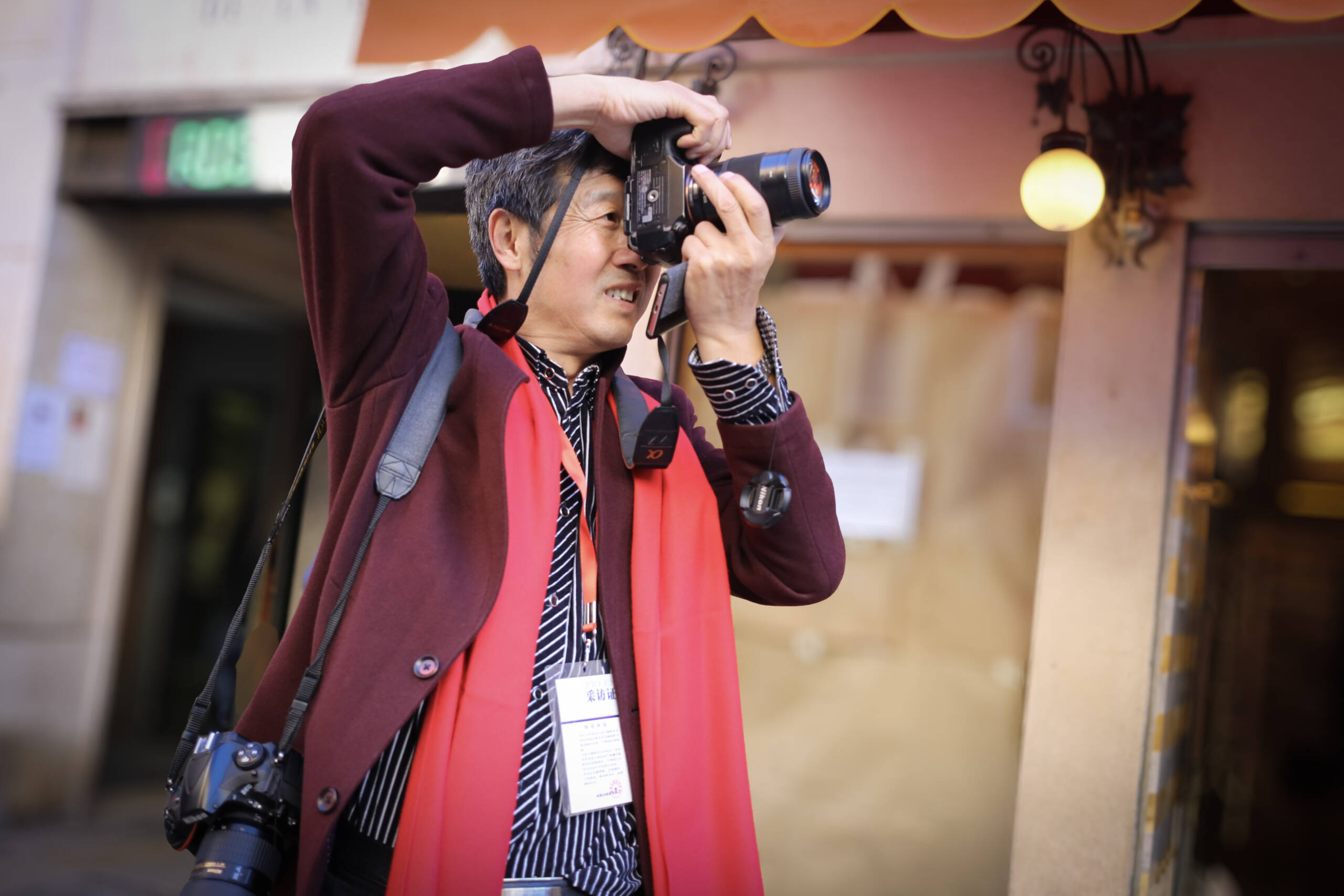 Photographer working a street with a Nikon DSLR, a second body on his hip and a press credential on a lanyard