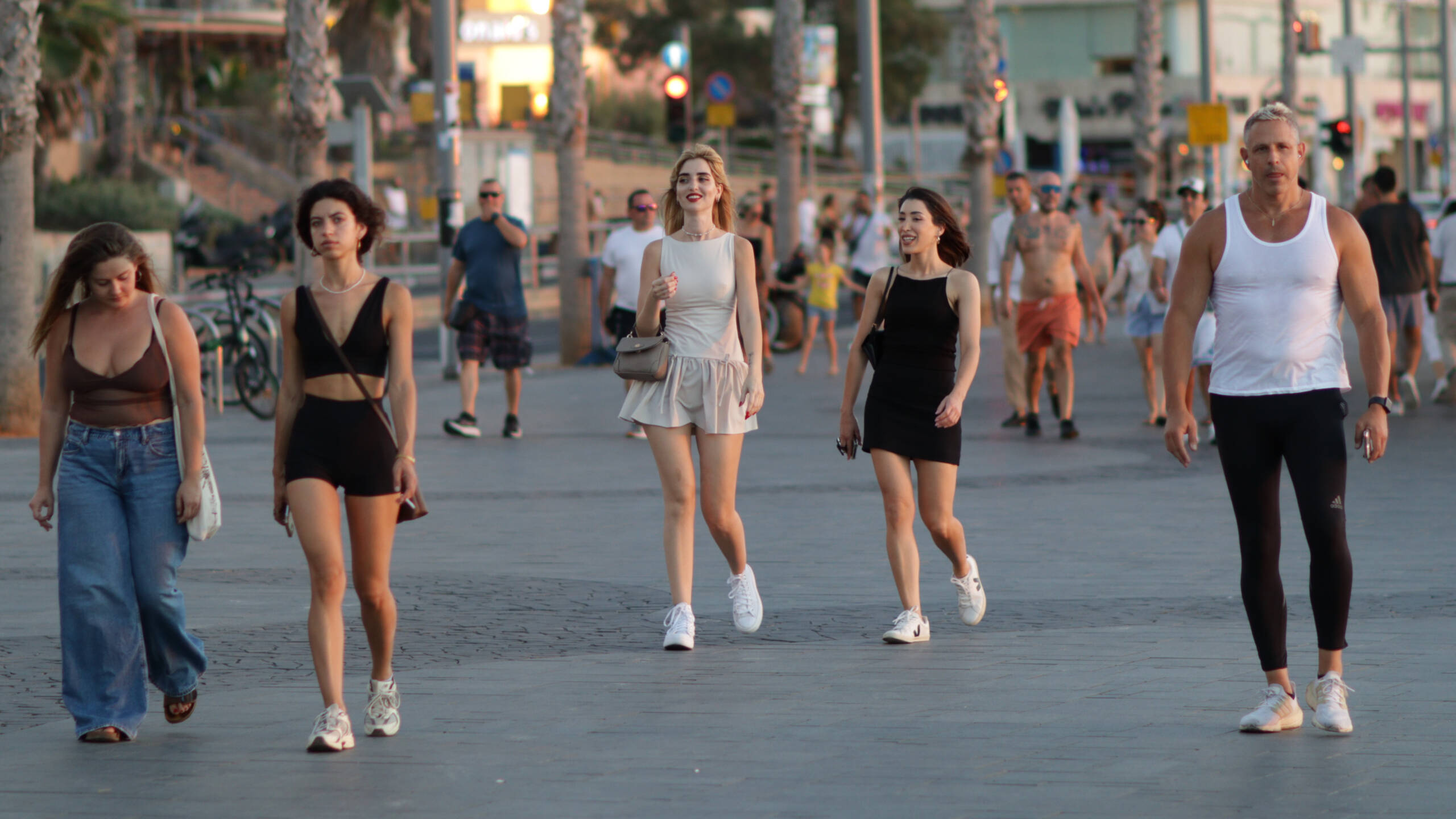Five people walking toward the camera along a seafront promenade in low golden light